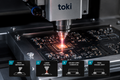 Toki laser solder paste soldering machine on a circuit board with process steps displayed.